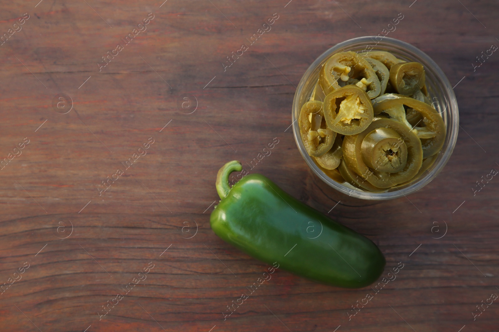 Photo of Fresh and pickled green jalapeno peppers on wooden table, flat lay. Space for text