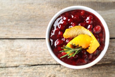 Photo of Fresh cranberry sauce in bowl, rosemary and orange peel on wooden table, top view. Space for text