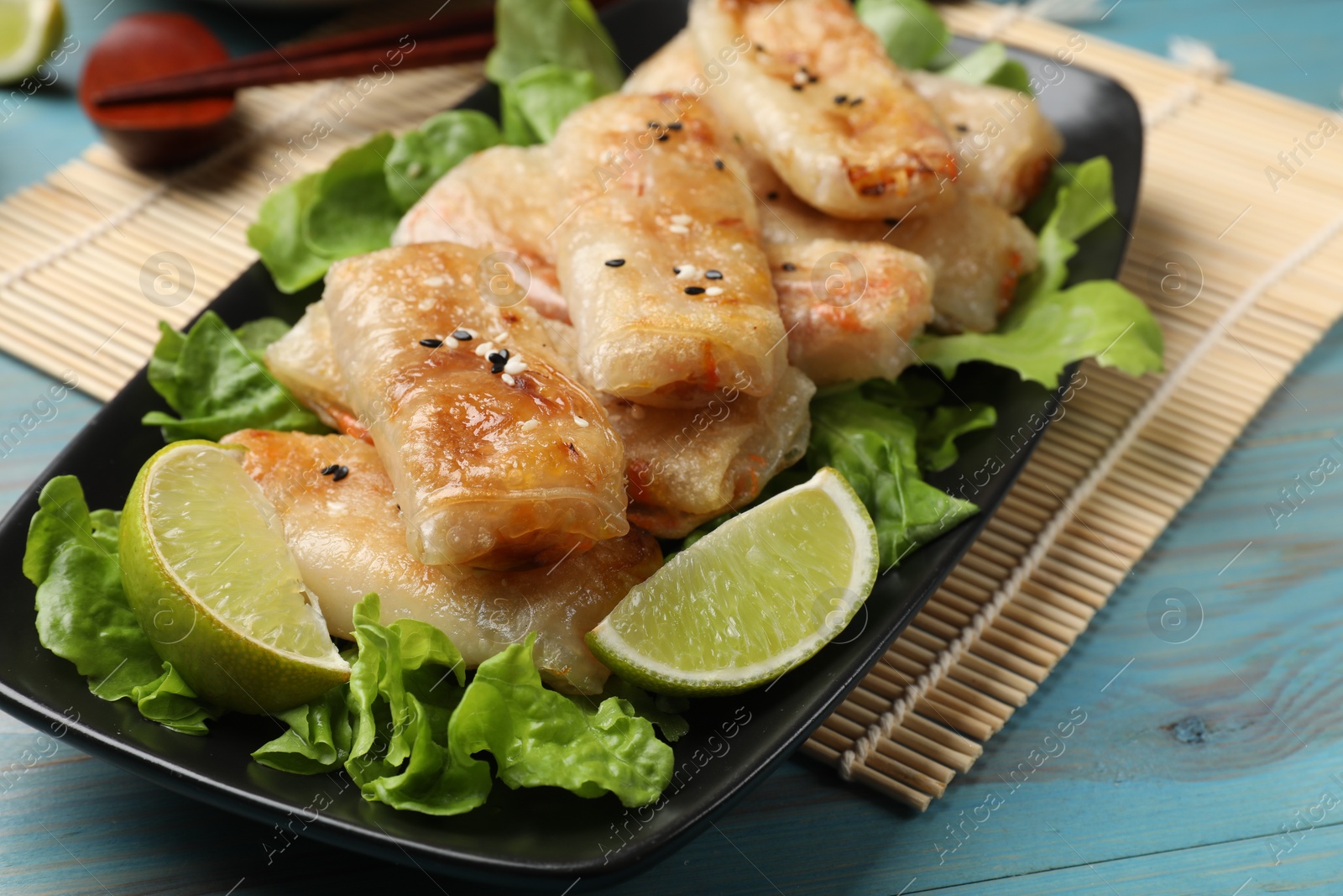 Photo of Tasty fried spring rolls, lettuce and lime on light blue wooden table, closeup