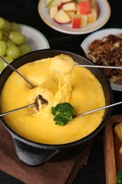 Photo of Dipping different products into fondue pot with melted cheese on table, above view