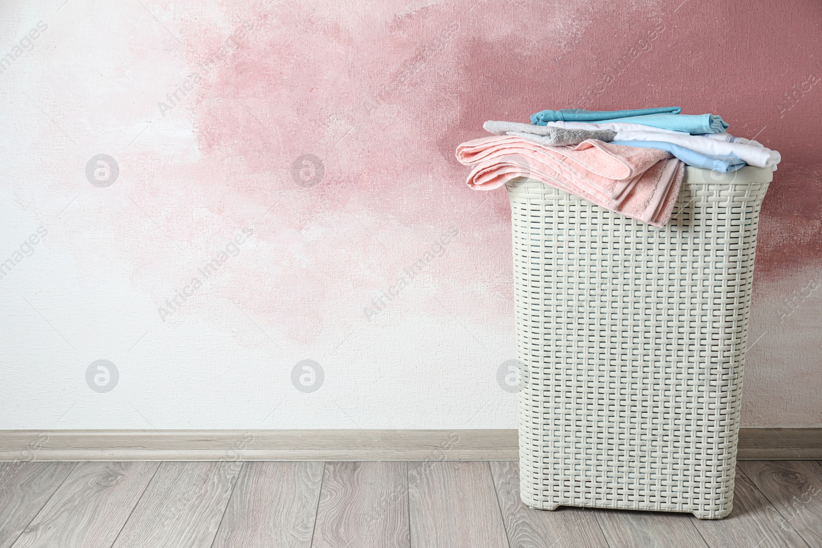 Photo of Basket with clean laundry on wooden floor near pink wall, space for text