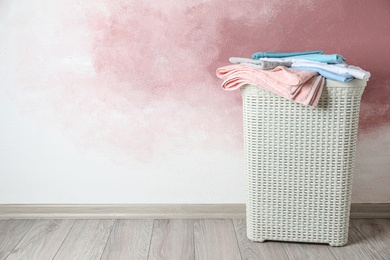 Basket with clean laundry on wooden floor near pink wall, space for text