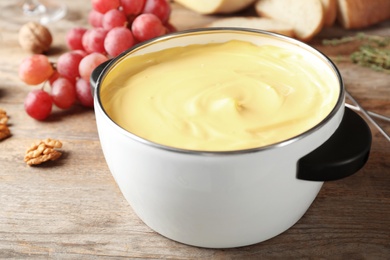 Photo of Pot with delicious cheese fondue on wooden table