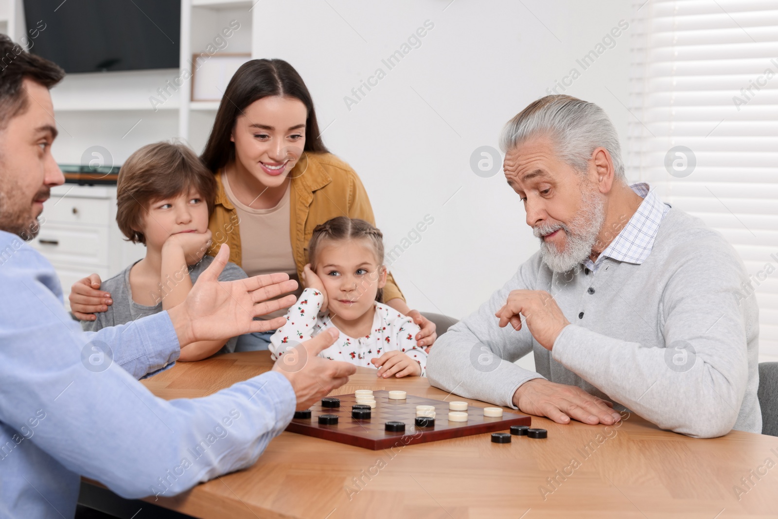 Photo of Happy family playing checkers at table in room