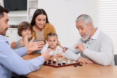 Photo of Happy family playing checkers at table in room