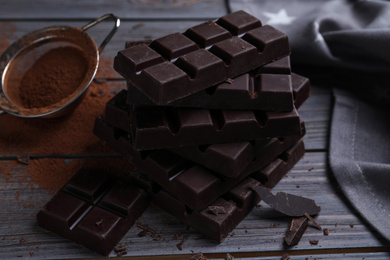 Photo of Tasty dark chocolate bars and sieve with cocoa powder on wooden table