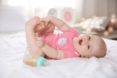 Photo of Pretty baby lying with bottle on bed at home