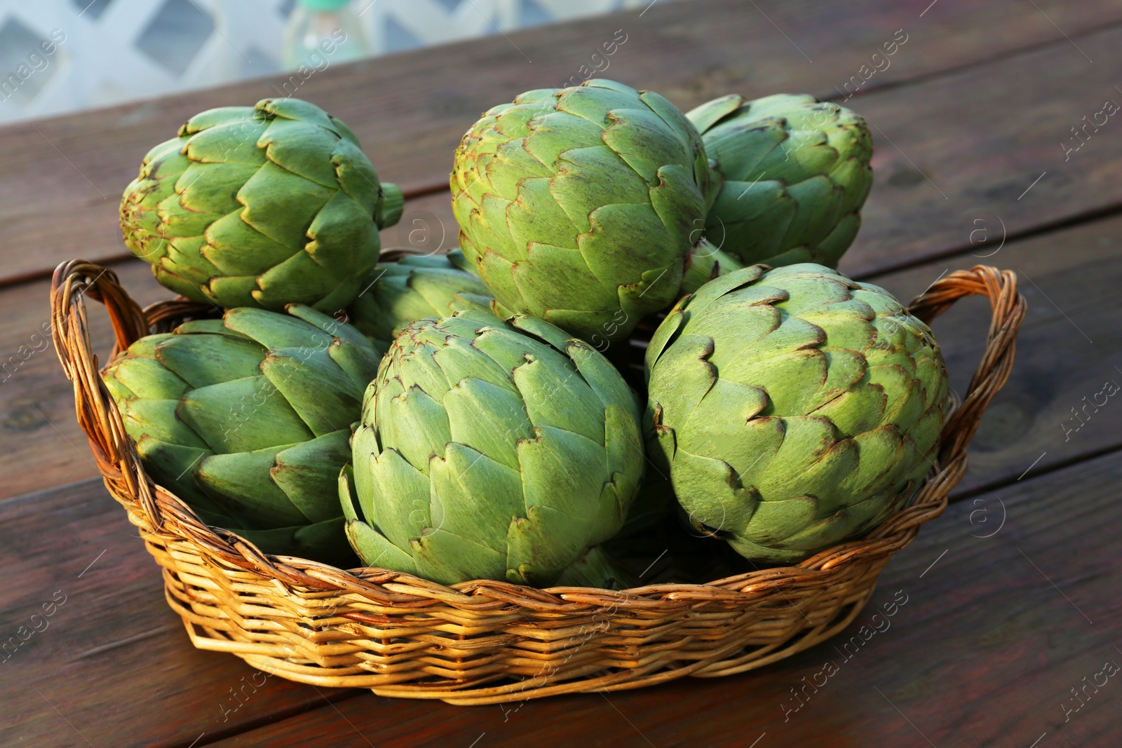 Photo of Wicker basket with fresh raw artichokes on wooden table