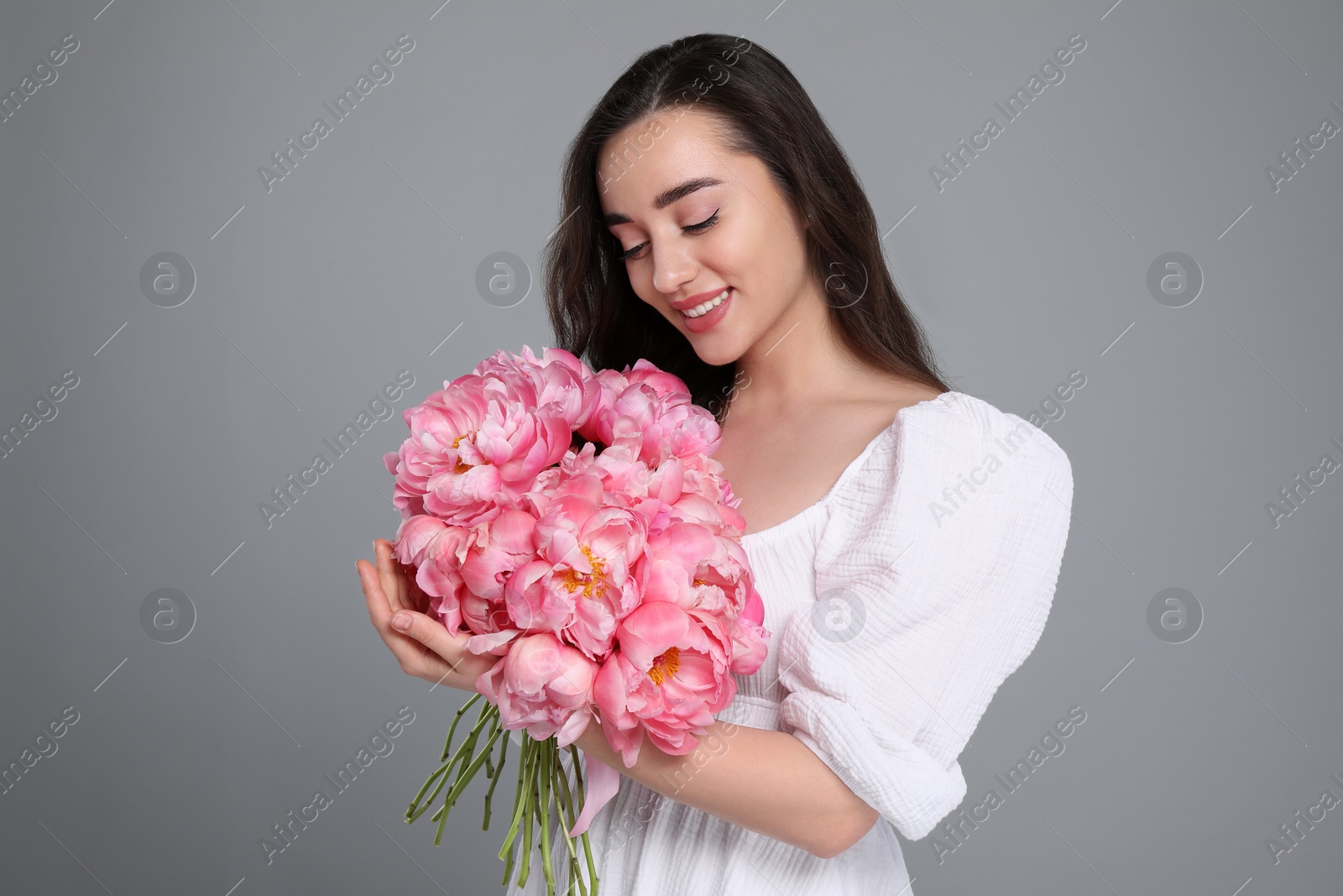 Photo of Beautiful young woman with bouquet of pink peonies on grey background