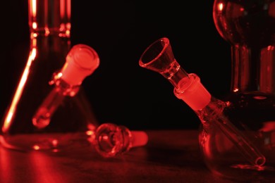 Photo of Glass bongs on table against black background, toned in red. Smoking device