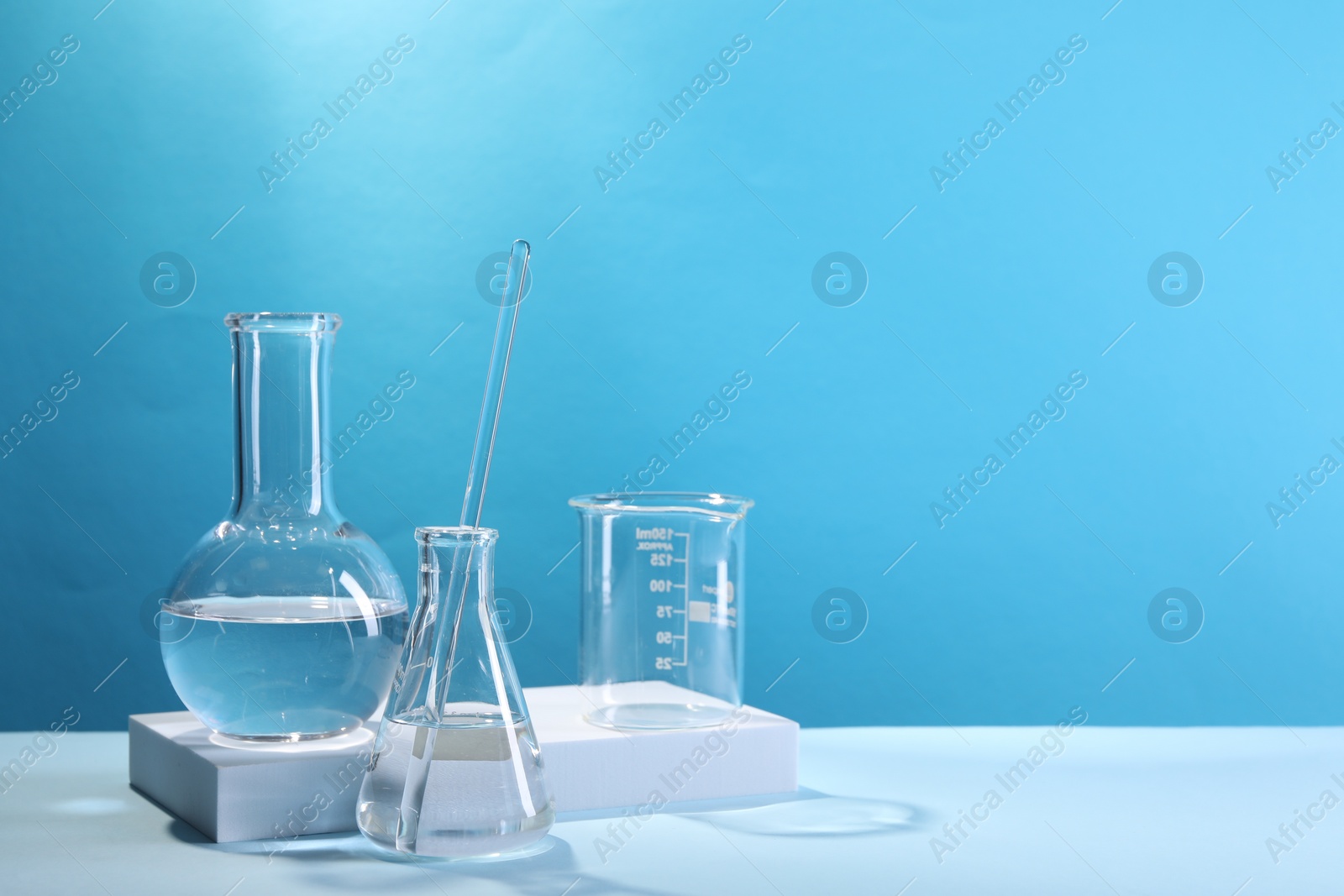 Photo of Laboratory analysis. Different glassware on table against light blue background, space for text