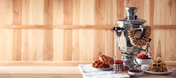 Photo of Traditional Russian samovar and treats on wooden table. Space for text