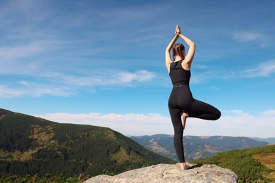 Photo of Young woman practicing outdoor yoga in mountains, back view. Fitness lifestyle