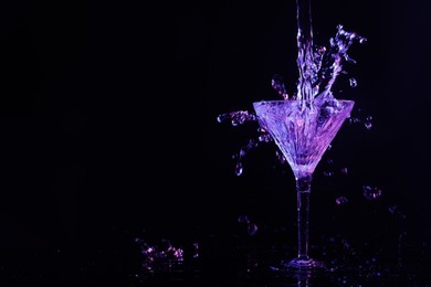 Photo of Pouring martini. Glass and splashes in neon lights on dark background. Space for text
