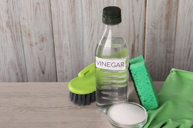 Photo of Natural cleaning products. Vinegar in bottle, baking soda, glove, sponge and brush on light wooden table. Space for text