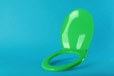 Photo of New green plastic toilet seat on light blue background, space for text