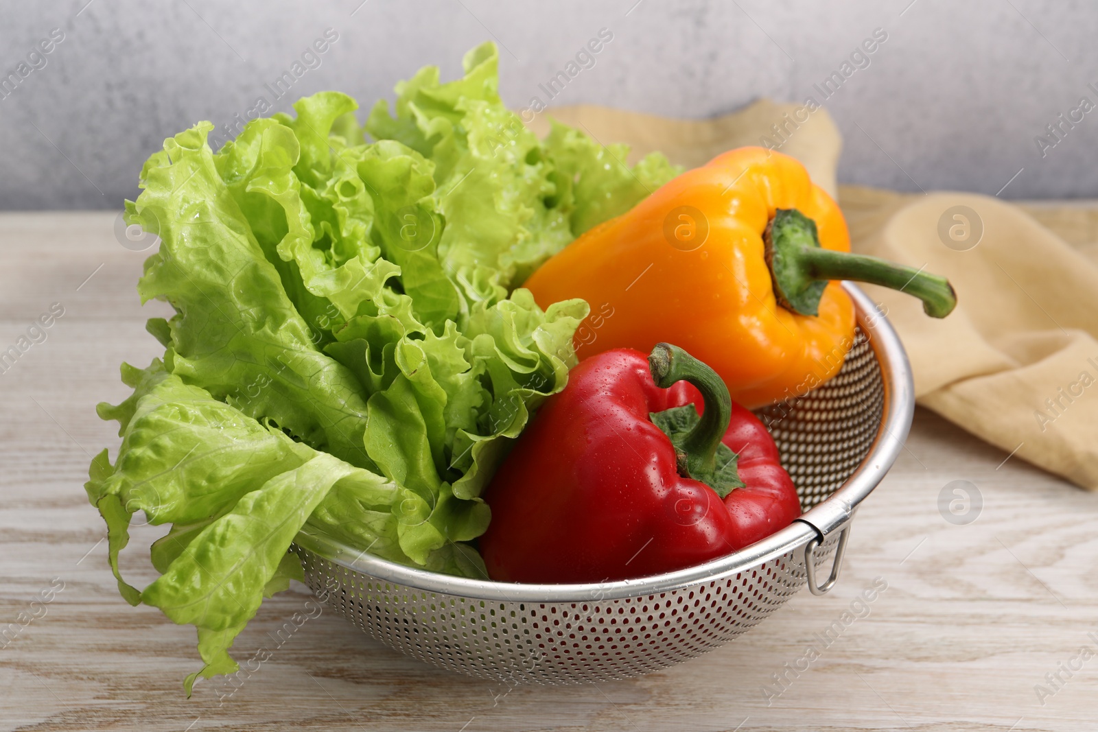 Photo of Colander with fresh lettuce and bell peppers on wooden table