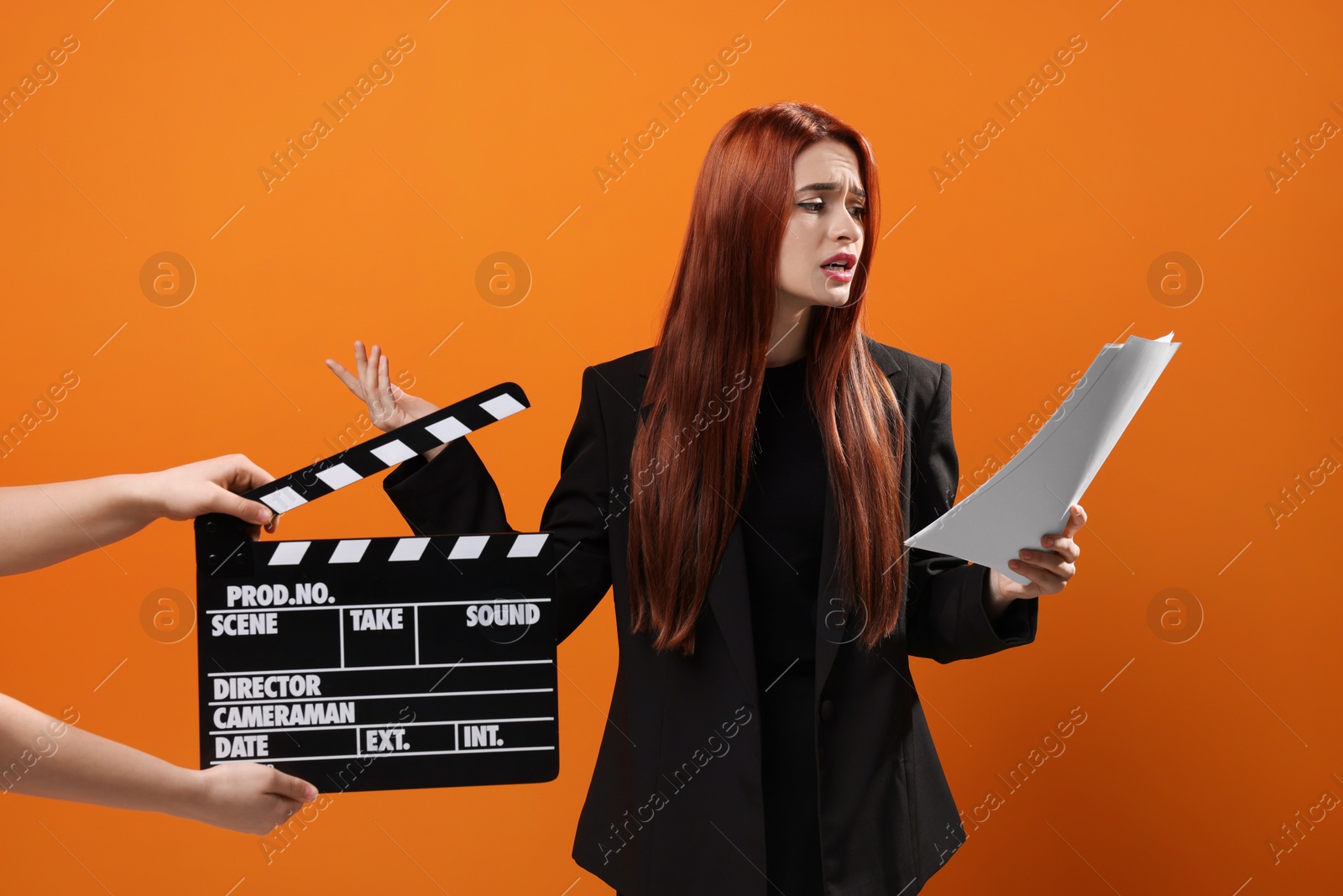 Photo of Actress performing role while second assistant camera holding clapperboard on orange background