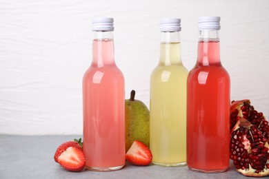 Delicious kombucha in glass bottles and fresh fruits on grey table against white background