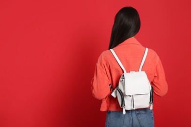 Photo of Young woman with stylish leather backpack on red background, back view. Space for text