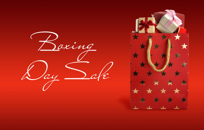 Boxing day sale. Shopping bag with gifts on red background