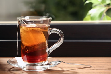 Photo of Glass cup of hot tea on wooden window sill. Space for text