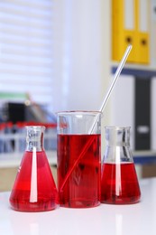 Photo of Laboratory analysis. Different glassware with red liquid on white table indoors