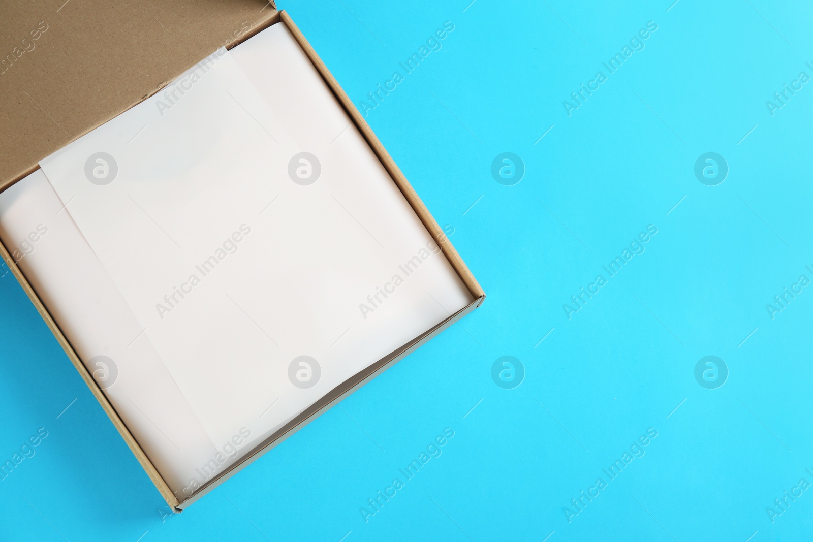 Photo of Open cardboard box on light blue background, top view. Space for text