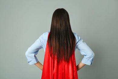 Photo of Young woman wearing superhero cape on light grey background, back view