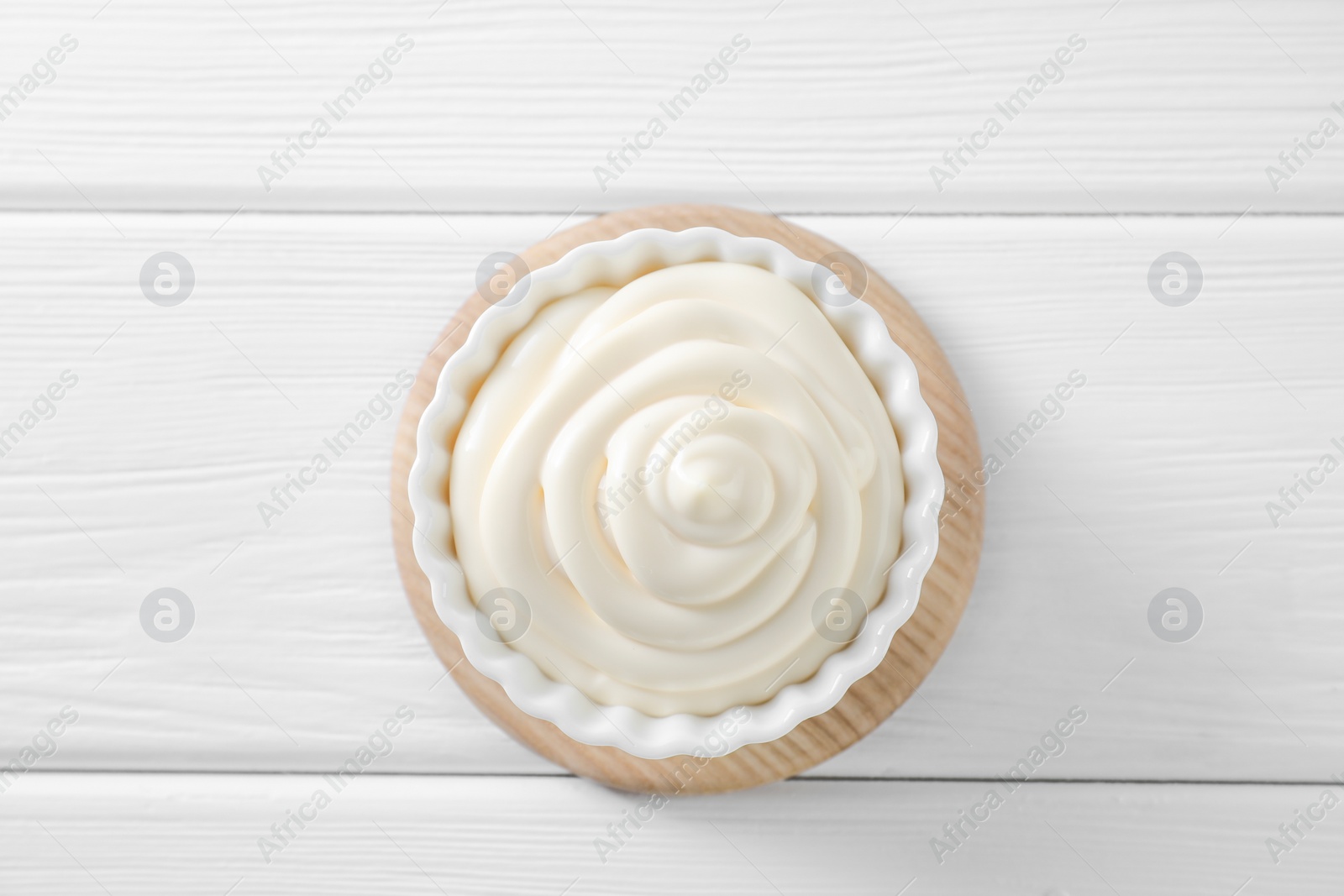 Photo of Fresh mayonnaise sauce in bowl on white wooden table, top view