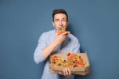 Photo of Attractive young man with delicious pizza on color background