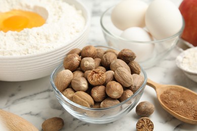 Photo of Nutmeg seeds and other ingredients for pastry on white marble table, closeup