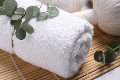 Photo of Spa composition with rolled towel and eucalyptus branches on grey table, closeup