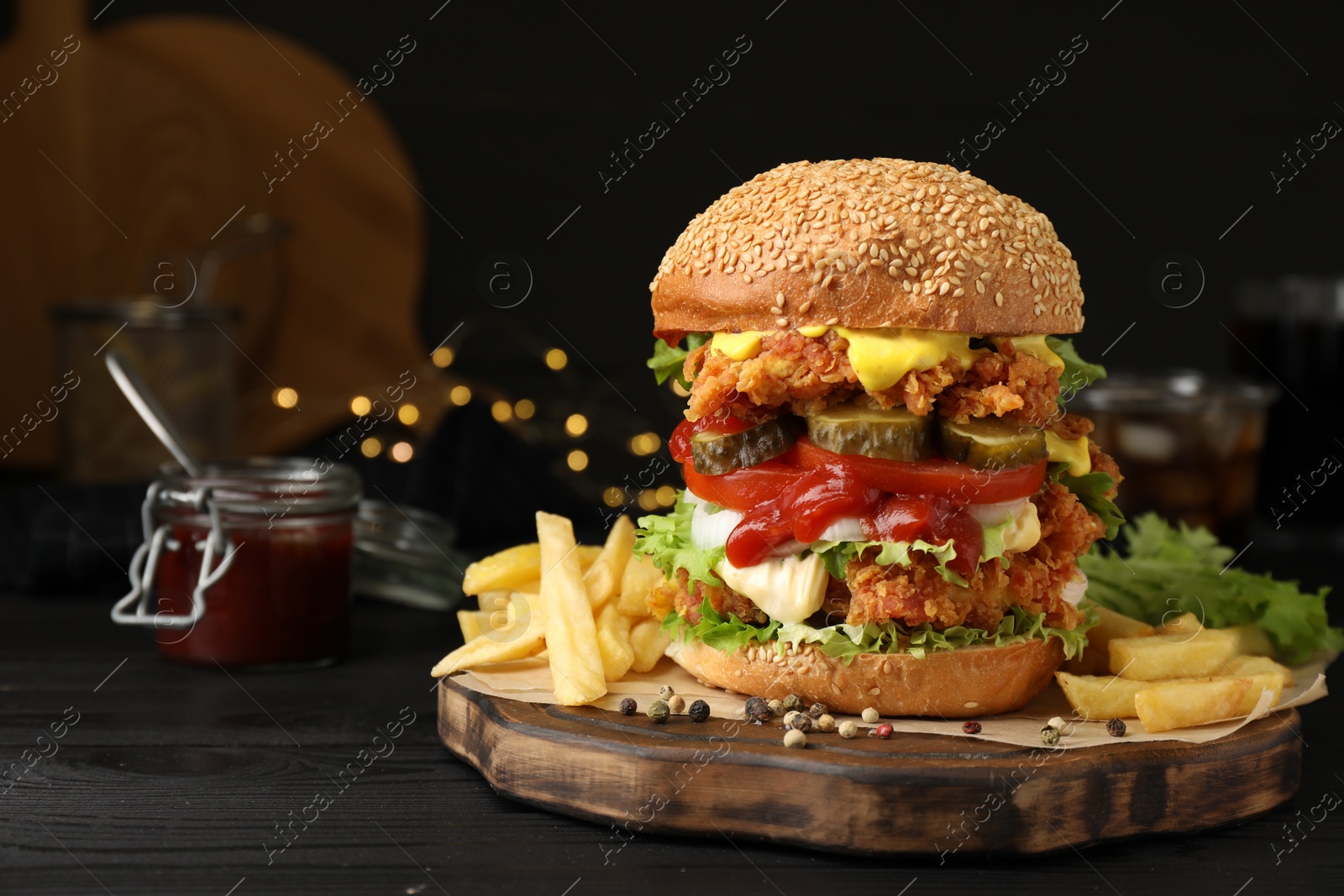 Photo of Delicious burger with crispy chicken patty and french fries on black wooden table