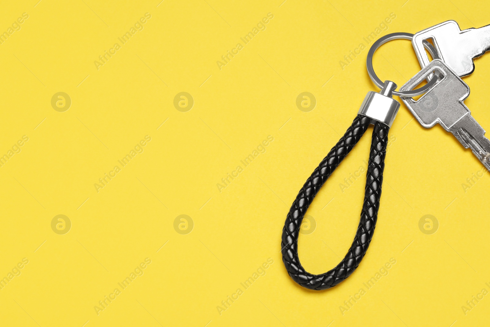 Photo of Keys with black leather keychain on yellow background, top view. Space for text