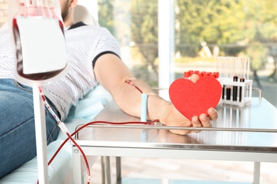 Man holding heart while making blood donation at hospital, closeup