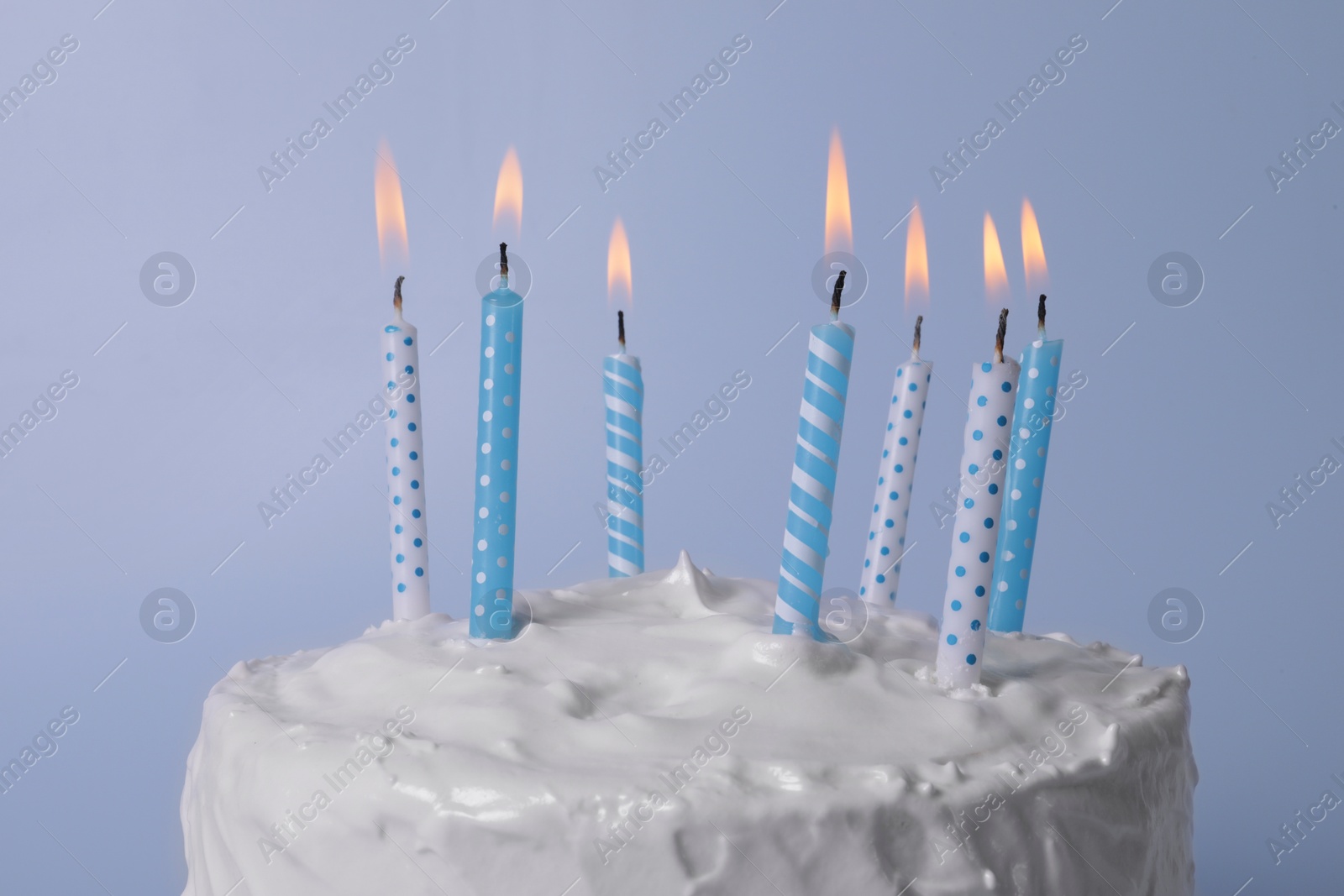 Photo of Delicious cake with cream and burning candles on light blue background, closeup