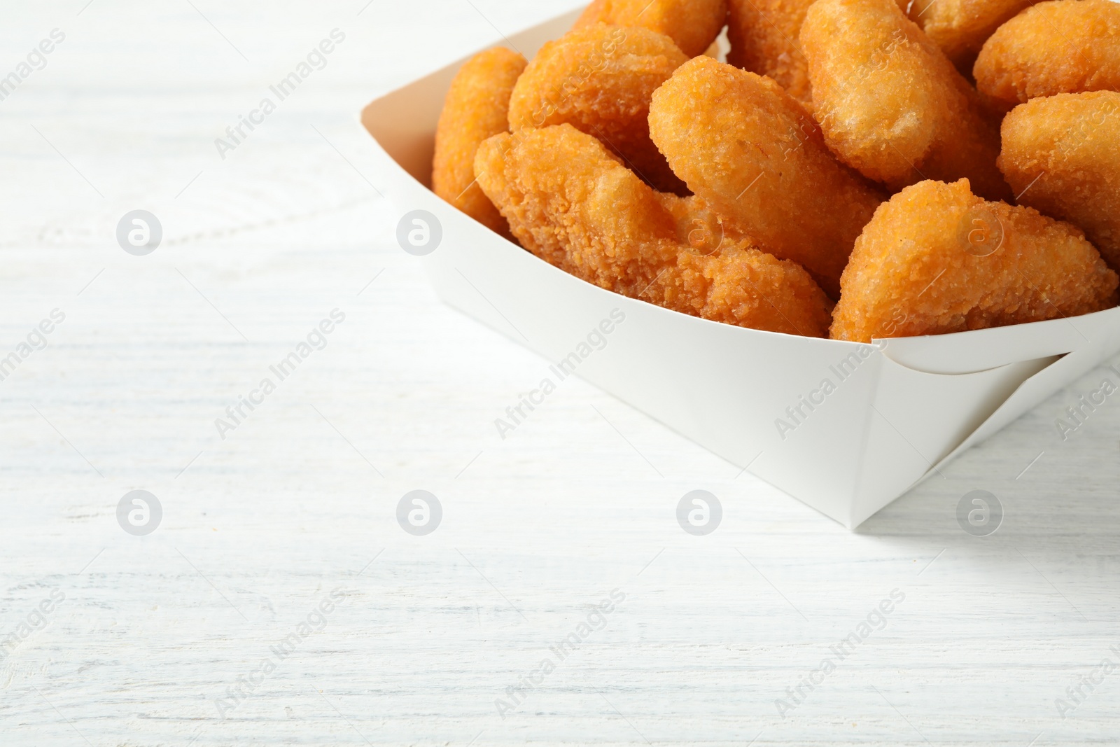 Photo of Tasty fried chicken nuggets on white wooden table, closeup. Space for text
