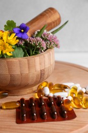 Photo of Mortar with fresh green herbs, flowers and pills on wooden board