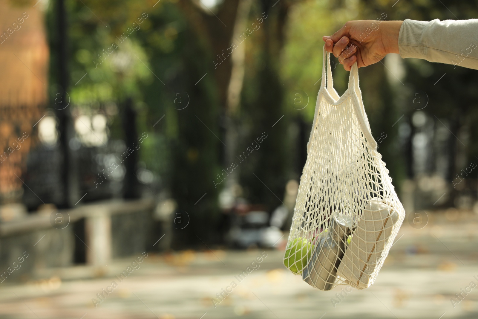 Photo of Conscious consumption. Woman with net bag of eco friendly products outdoors, closeup. Space for text