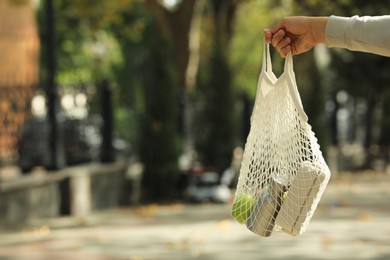 Photo of Conscious consumption. Woman with net bag of eco friendly products outdoors, closeup. Space for text