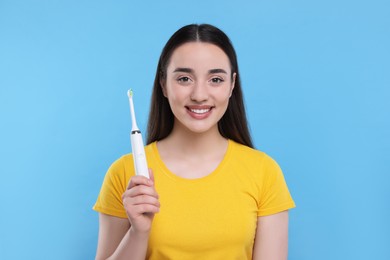 Happy young woman holding electric toothbrush on light blue background