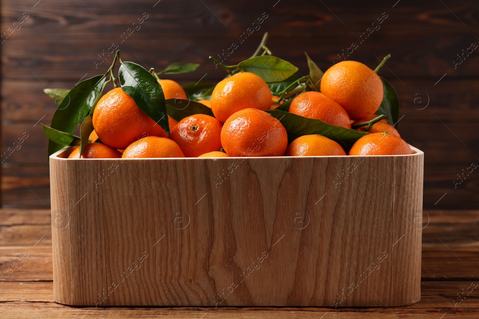 Photo of Fresh tangerines with green leaves in crate on wooden table