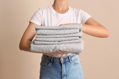 Photo of Woman holding stack of clean bed linens on beige background