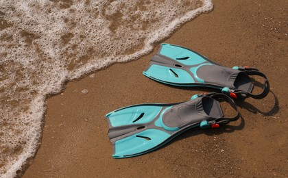 Pair of turquoise flippers on sand near sea