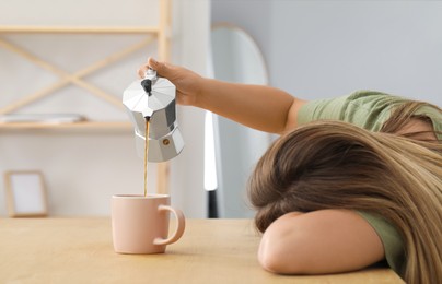 Photo of Sleepy woman pouring coffee into cup at wooden table indoors