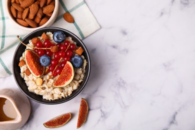 Photo of Bowl of oatmeal with berries, almonds and fig pieces on white marble table, flat lay. Space for text