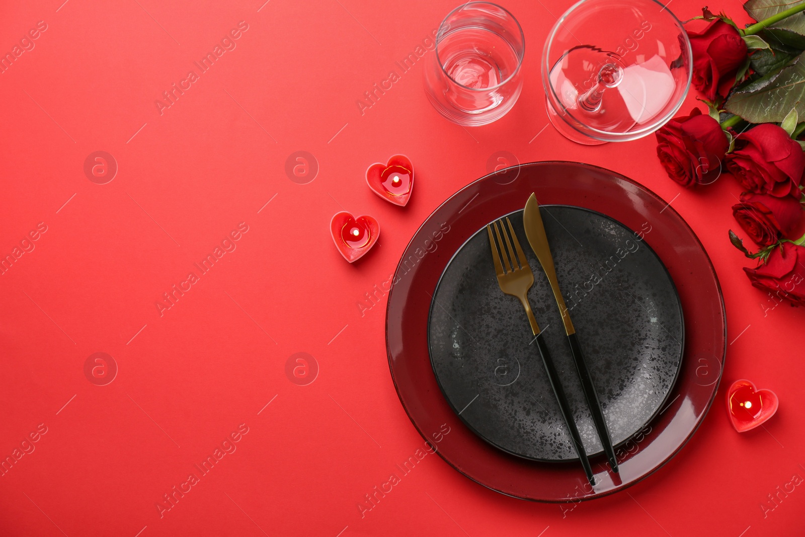 Photo of Place setting with heart shaped candles and bouquet of roses for romantic dinner on red table, flat lay. Space for text