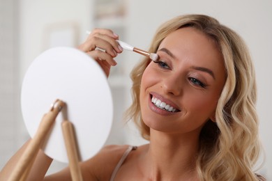 Photo of Beautiful makeup. Smiling woman applying eyeshadows in front of mirror indoors