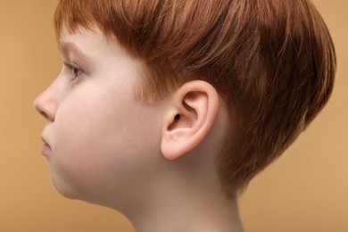 Photo of Hearing problem. Little boy on pale brown background, closeup